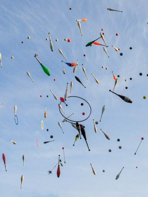 Vibrant juggling props in mid-air against a bright blue sky, showcasing motion and creativity.